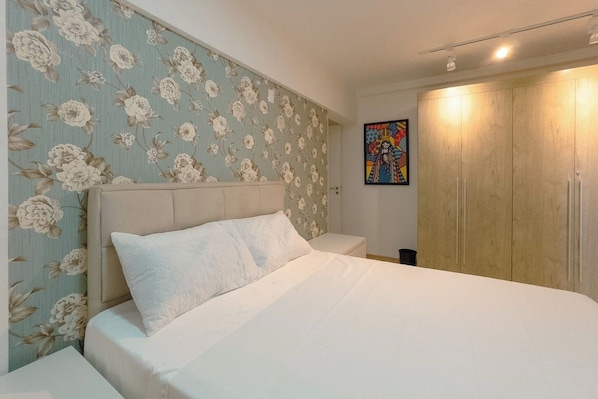 A bedroom with a bed, a nightstand, a wardrobe, and a floral wallpaper.