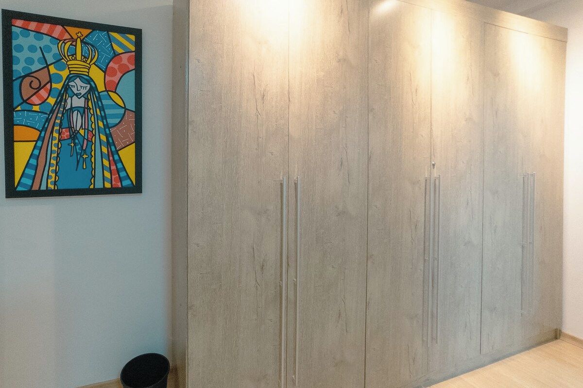 Una habitación con un armario grande, un cubo pequeño de basura y un cuadro colorido en la pared.