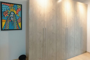 Ein Zimmer mit einem großen Kleiderschrank, einer kleinen Mülltonne und einem farbenfrohen Bild an der Wand.