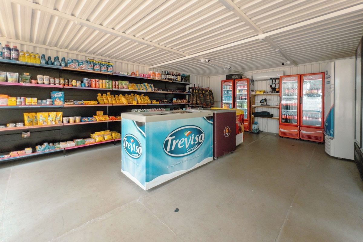 L’intérieur d’un magasin, avec des étagères remplies de divers produits alimentaires, un comptoir orné d’une enseigne de marque et deux distributeurs de boissons rouges.