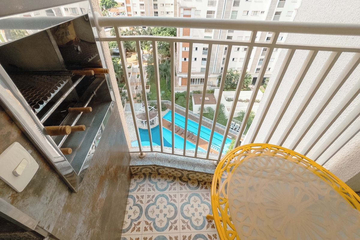Varanda com churrasqueira, vista para piscina e piso estampado.