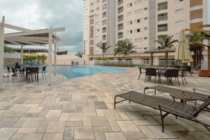 A pool area with lounge chairs and umbrellas, surrounded by a high-rise building.