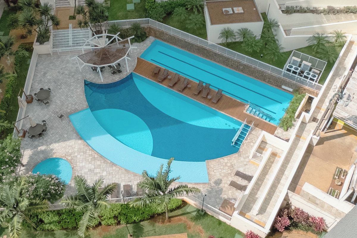 A large swimming pool with a sun deck, surrounded by palm trees and a patio area with outdoor seating.