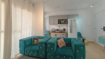 Una sala moderna con un conjunto de sofá color turquesa, una cocina al fondo y una puerta a la derecha.