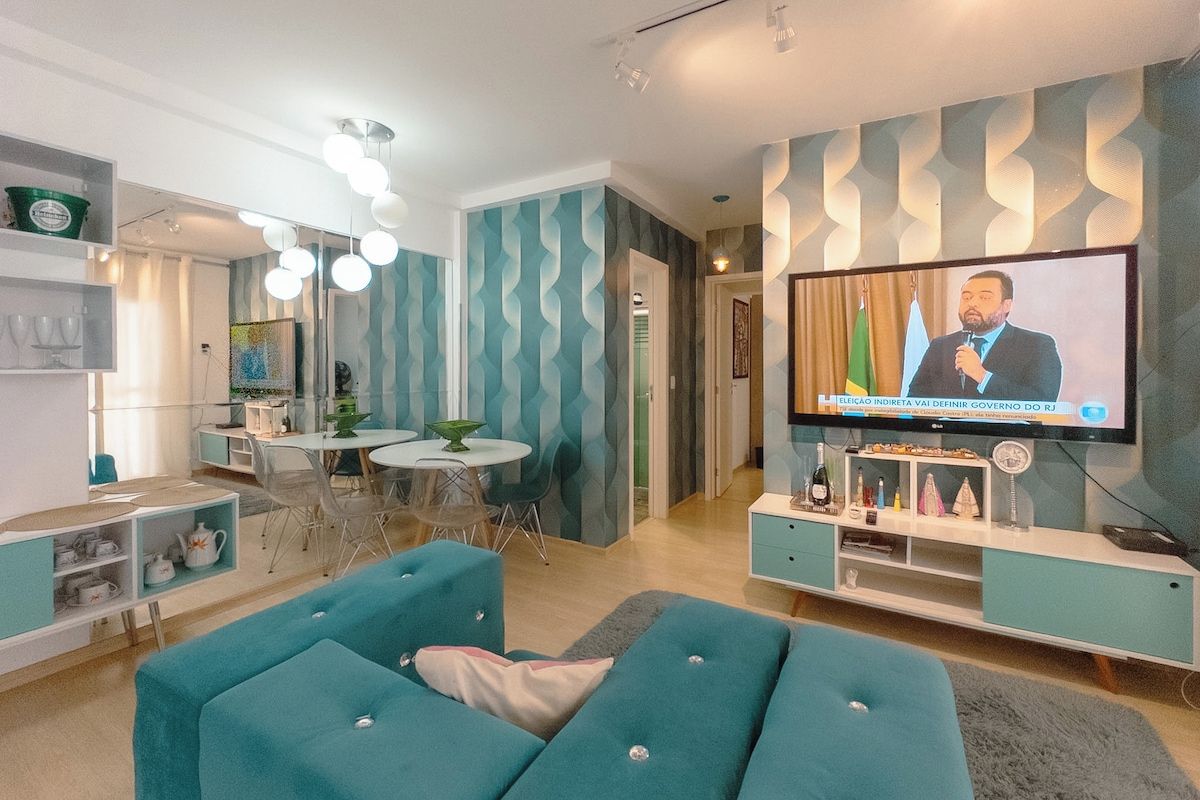 A living room with a television displaying a news broadcast, a dining area with a table and chairs, and a seating area with sofas.