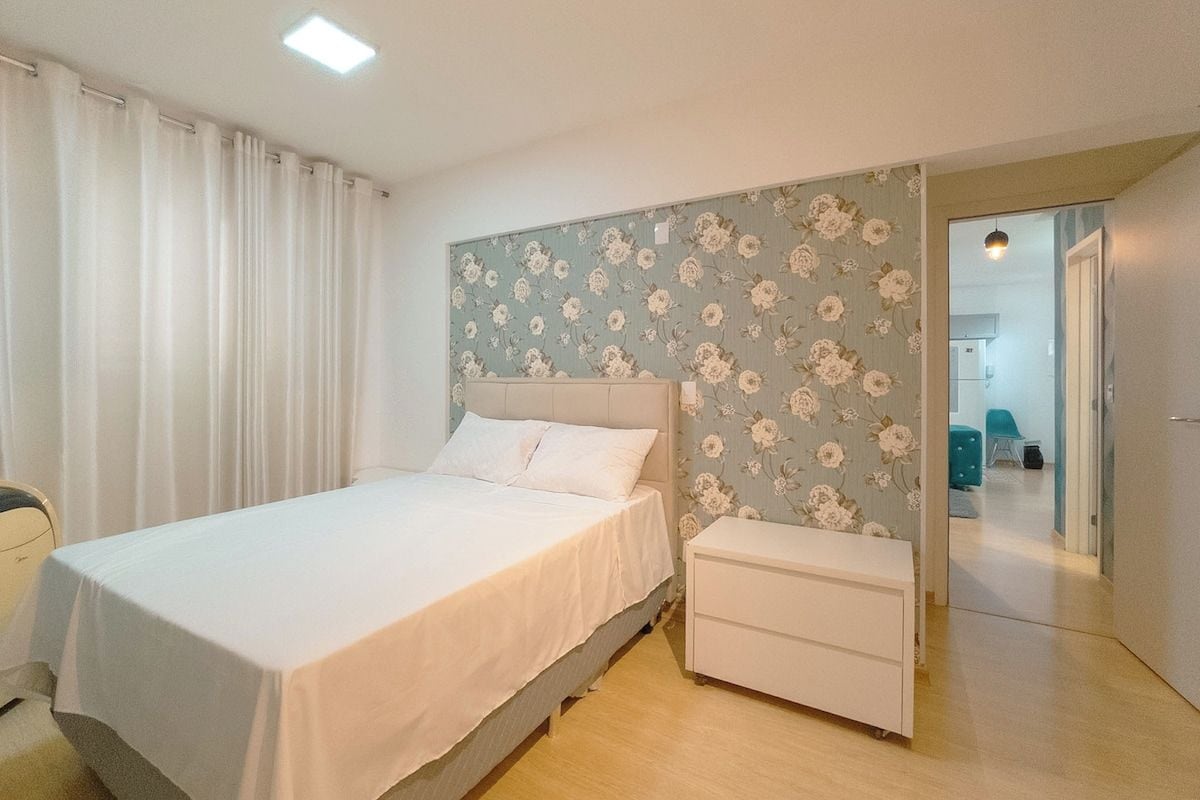 Een slaapkamer met een bed, een nachtkastje en een wand met bloemenbehang.