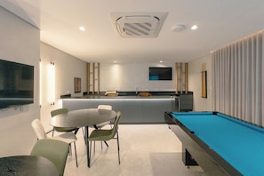 Een moderne kamer met een pooltafel, een eethoek met stoelen, een bar en een aan de muur bevestigde televisie.