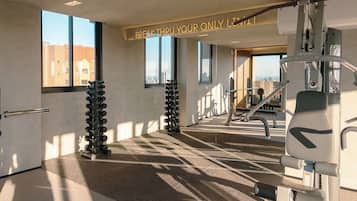 Ein Fitnessstudio mit Trainingsgeräten, einem motivierenden Spruch und großen Fenstern.