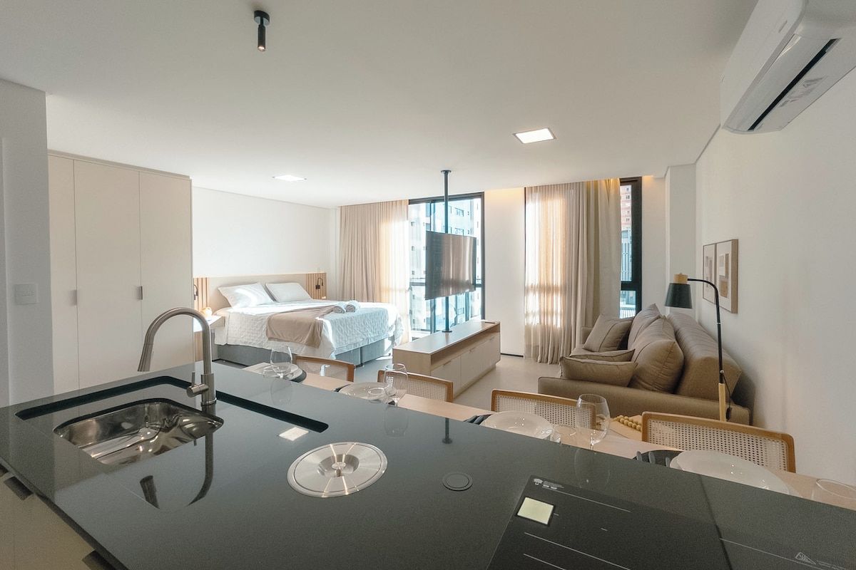 A modern hotel room with a kitchenette, a bed, a sofa, and a TV.