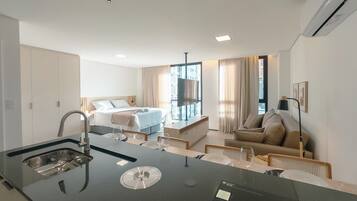 A modern hotel room with a kitchenette, a bed, a sofa, and a TV.