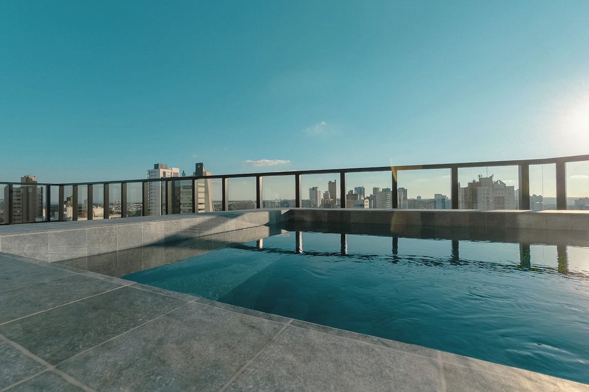 Piscina no terraço com vista para a cidade, cercada por guarda-vidro de vidro.