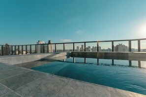 Piscina no terraço com vista para a cidade, cercada por guarda-vidro de vidro.