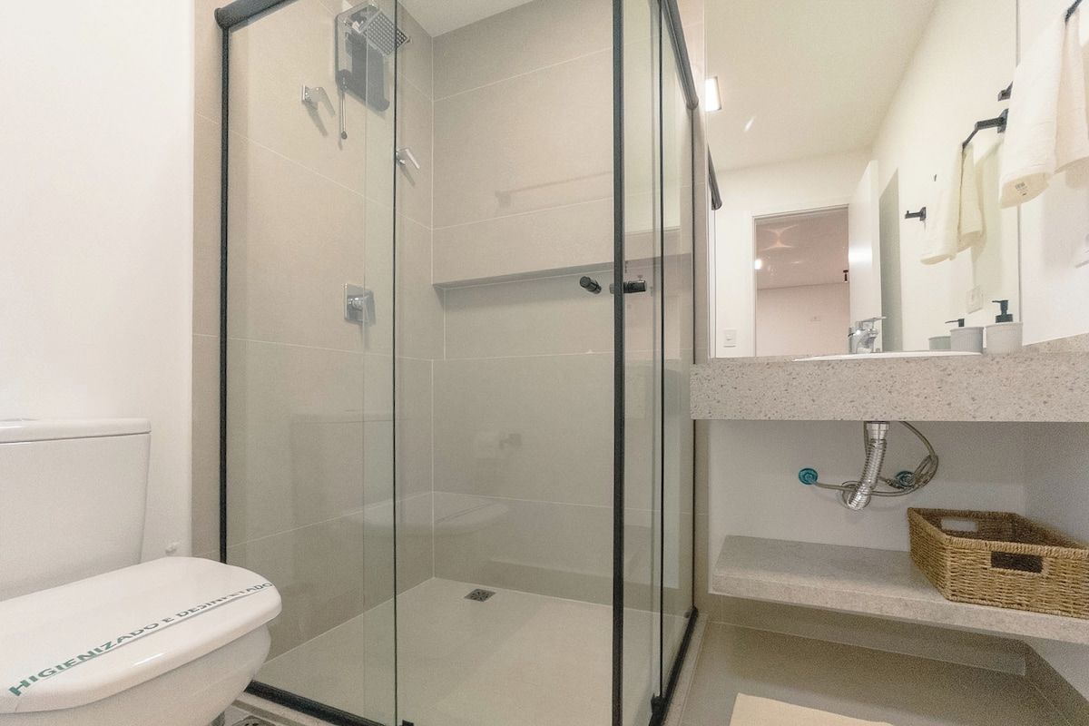 Uma casa de banho moderna com cabine de duche em vidro, sanita e toucador com lavatório e espelho.