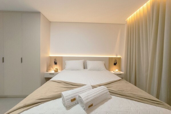 Una habitación de hotel con una cama grande, mesitas de noche, un armario y una cortina.