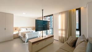 Quarto de hotel com uma cama, televisão em móvel, sofá e janela com cortinas.