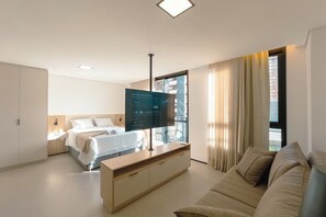 Een hotelkamer met een bed, een televisie op een standaard, een bank en een raam met gordijnen.