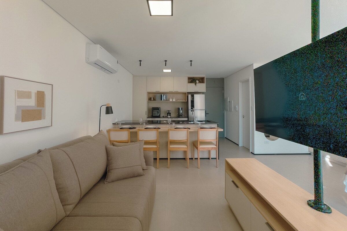 Uma sala de estar moderna com sofá, televisão de tela plana e área de cozinha com mesa e cadeiras.