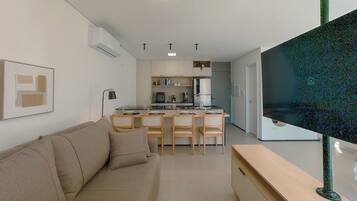 Uma sala de estar moderna com sofá, televisão de tela plana e área de cozinha com mesa e cadeiras.