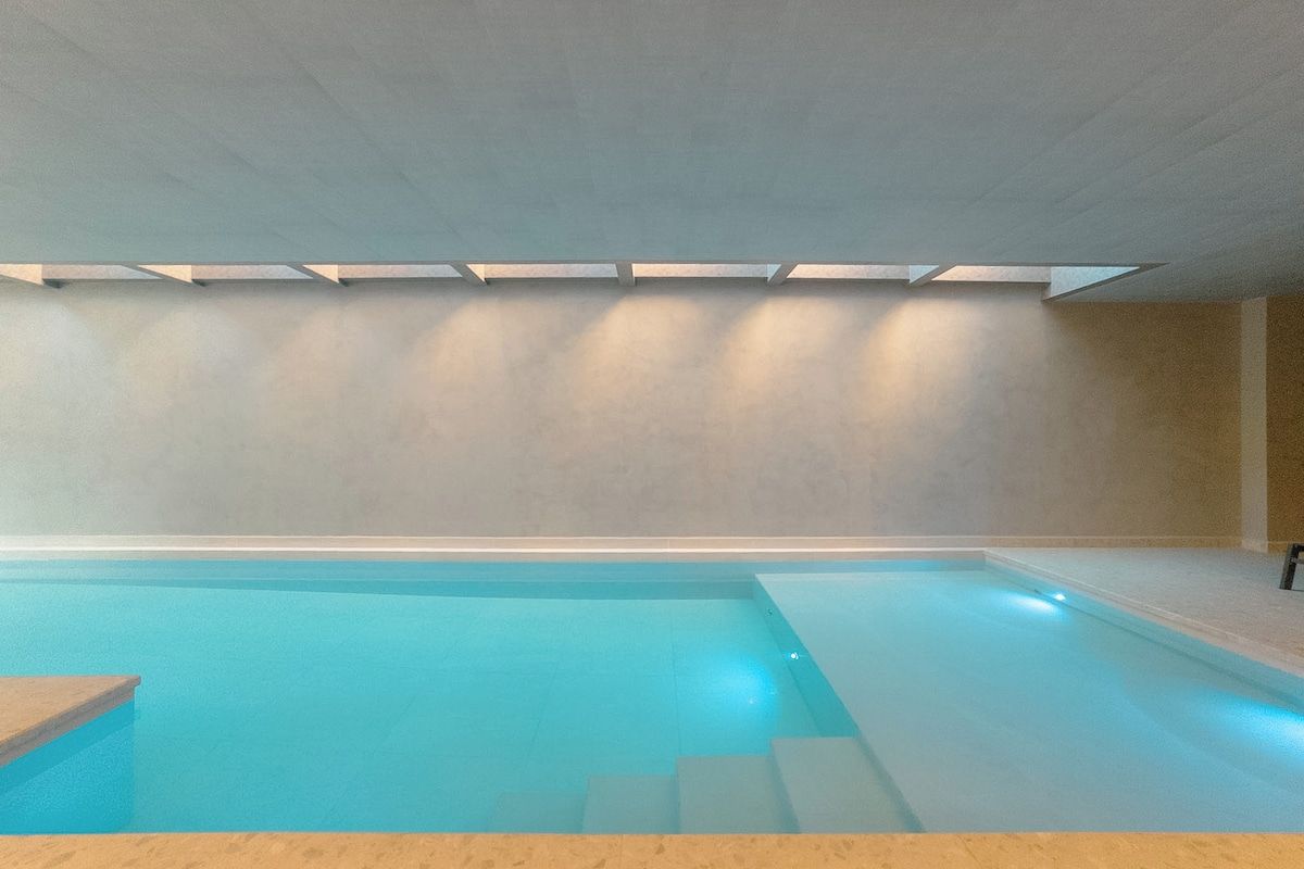 Piscina com superfície de água azul cristalina, um deck ladrilhado ao redor e uma clarabóia acima.