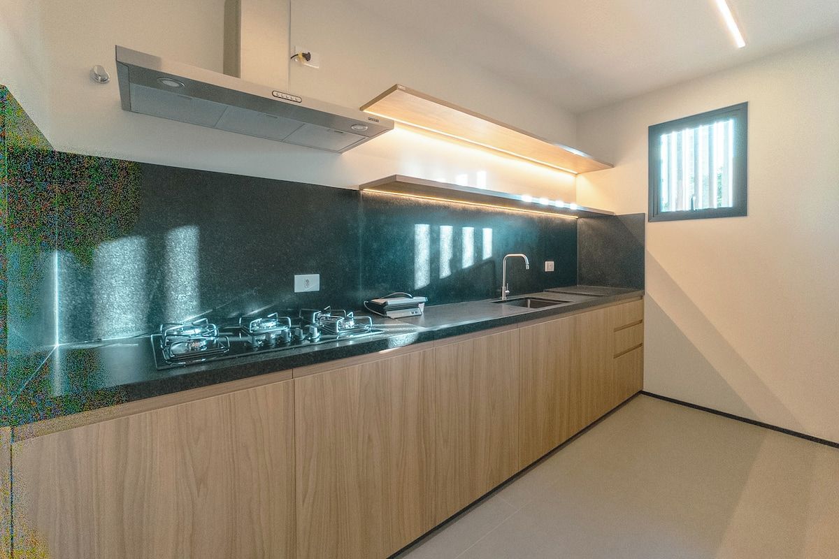 Eine moderne Küche mit schwarzem Arbeitsplatz, Holzschränken, einer Edelstahl-Dunstabzugshaube und einem Fenster, das für natürliches Licht sorgt.