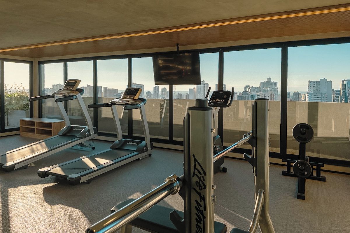 Ein Fitnessstudio mit Laufbändern, Kraftgeräten und Blick auf die Stadt durch große Fenster.
