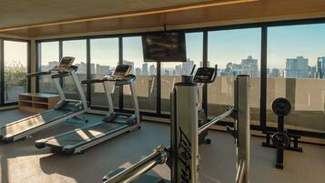 Ein Fitnessstudio mit Laufbändern, Kraftgeräten und Blick auf die Stadt durch große Fenster.
