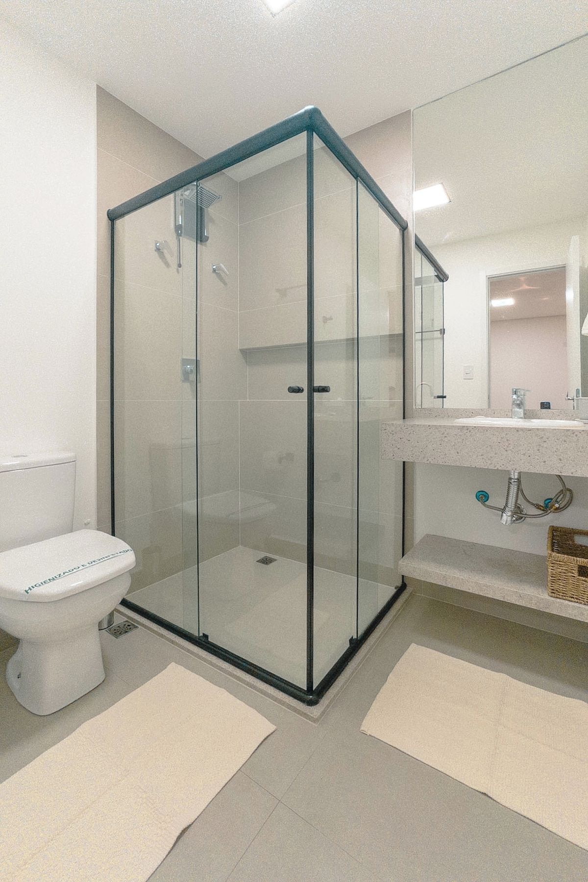 Een moderne badkamer met een douchecabine van glas, een wit toilet en een wastafel met een spiegel erboven.
