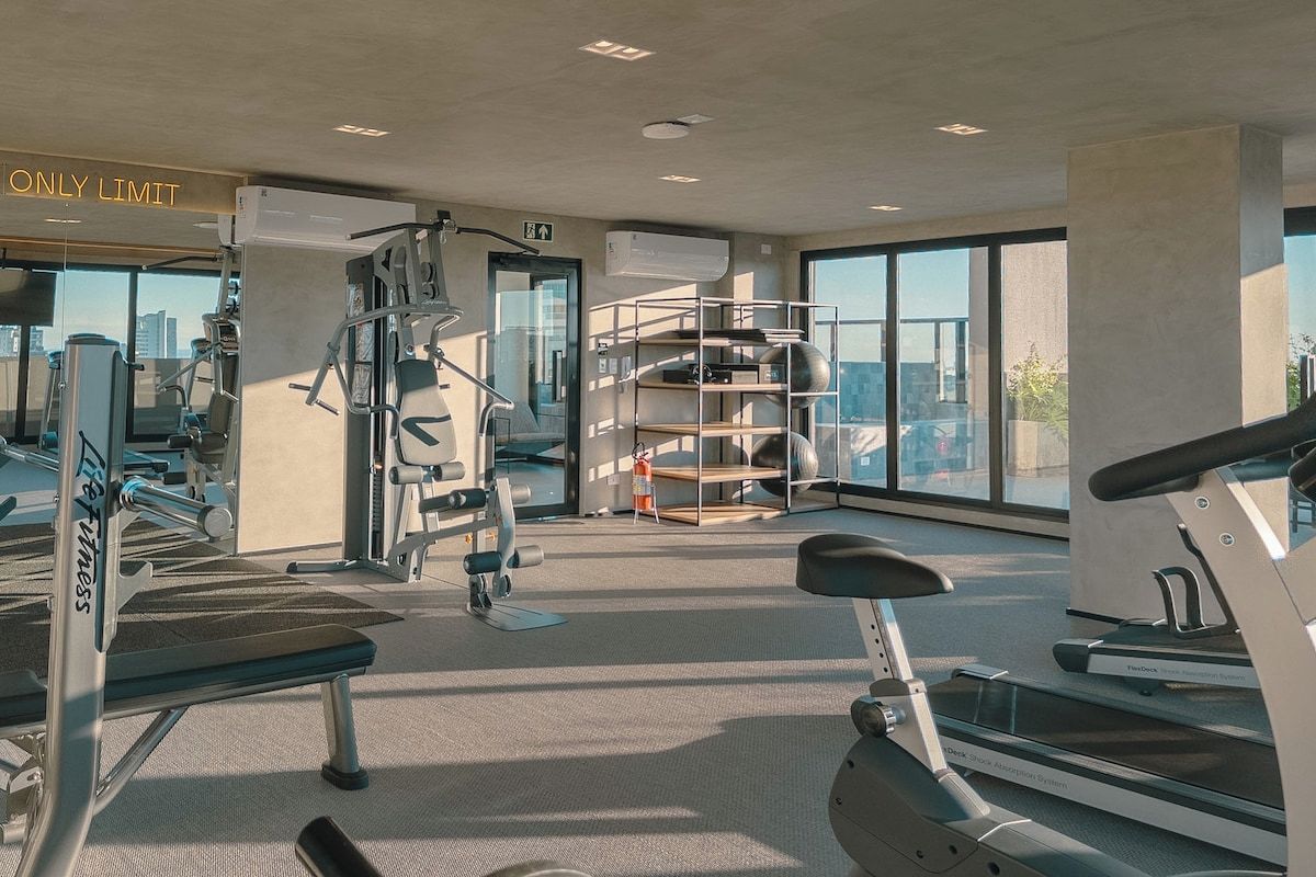 Academia moderna com diversos equipamentos de exercício, um banco e esteira.
