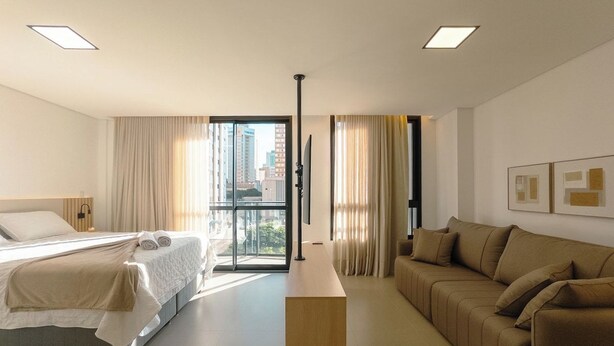 Quarto de hotel com cama, sofá, escrivaninha e vista para a cidade.