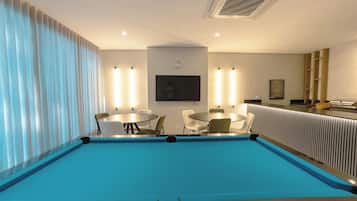 Un espace piscine avec une piscine bleue, des chaises blanches, une table et un téléviseur fixé au mur.