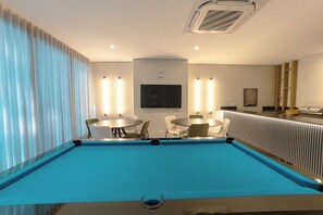 A pool area with a blue pool, white chairs, a table, and a TV mounted on the wall.