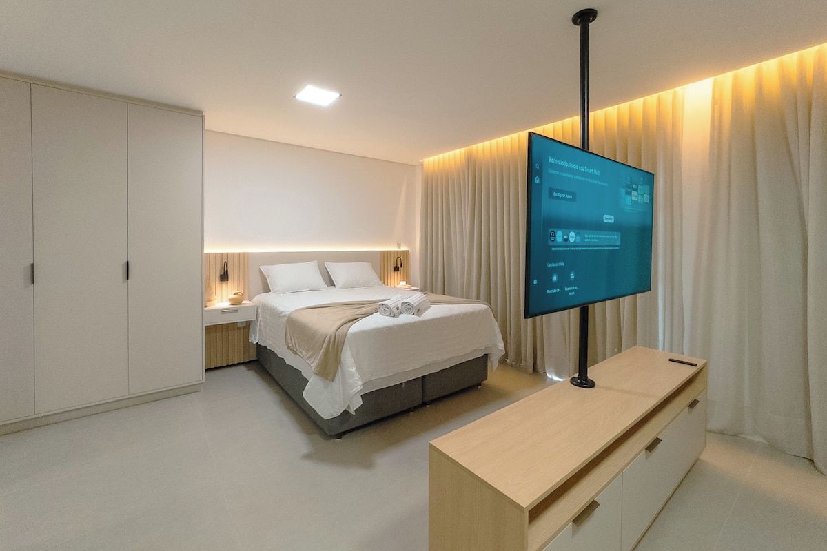 Quarto de hotel moderno com cama, mesa de cabeceira, televisão e guarda-roupa.