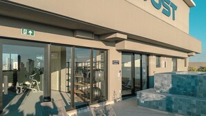 Um edifício com uma ampla entrada de vidro, uma placa com a inscrição 'JUST' e equipamentos de exercícios ao ar livre.