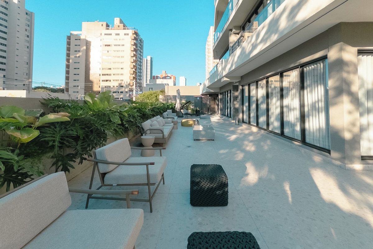 Área externa com sofás e vasos de plantas, um caminho e vista para a paisagem urbana.