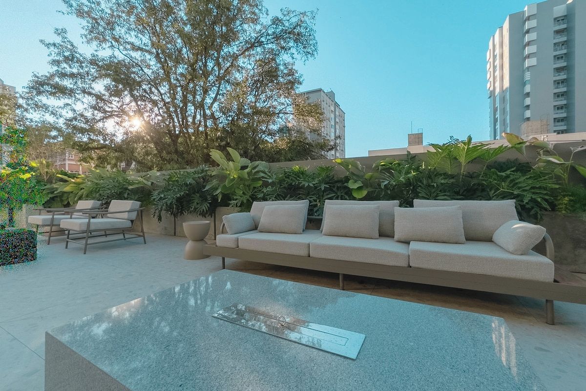 A modern outdoor seating area with a sofa and chairs, surrounded by greenery and a clear sky.