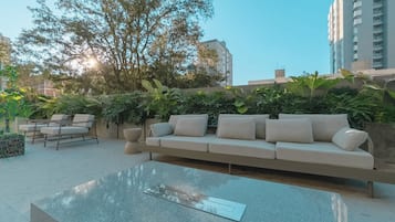 A modern outdoor seating area with a sofa and chairs, surrounded by greenery and a clear sky.