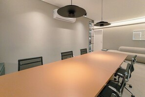 Un salón de conferencias con una larga mesa, sillas y un equipo de aire acondicionado instalado en el techo.