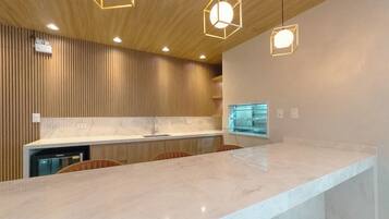 A modern kitchen with a marble countertop, wooden paneling, and pendant lighting.