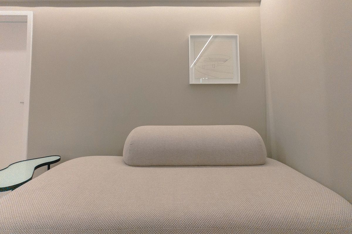 A minimalist room with a bed, a wall-mounted light fixture, and a door.