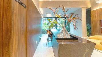 Interior moderno com parede de painéis de madeira, área de bar com banquetas e uma grande planta em vaso.