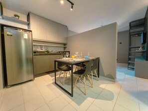 A modern kitchen with a stainless steel refrigerator, a dining table with chairs, and a built-in oven. - Modern Apartment near UEM with Wi-Fi - LP12 (Maringá)