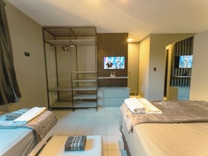 Ein Hotelzimmer mit zwei Betten, einem Schrank, einem Fernseher und einer kleinen Sitzecke.