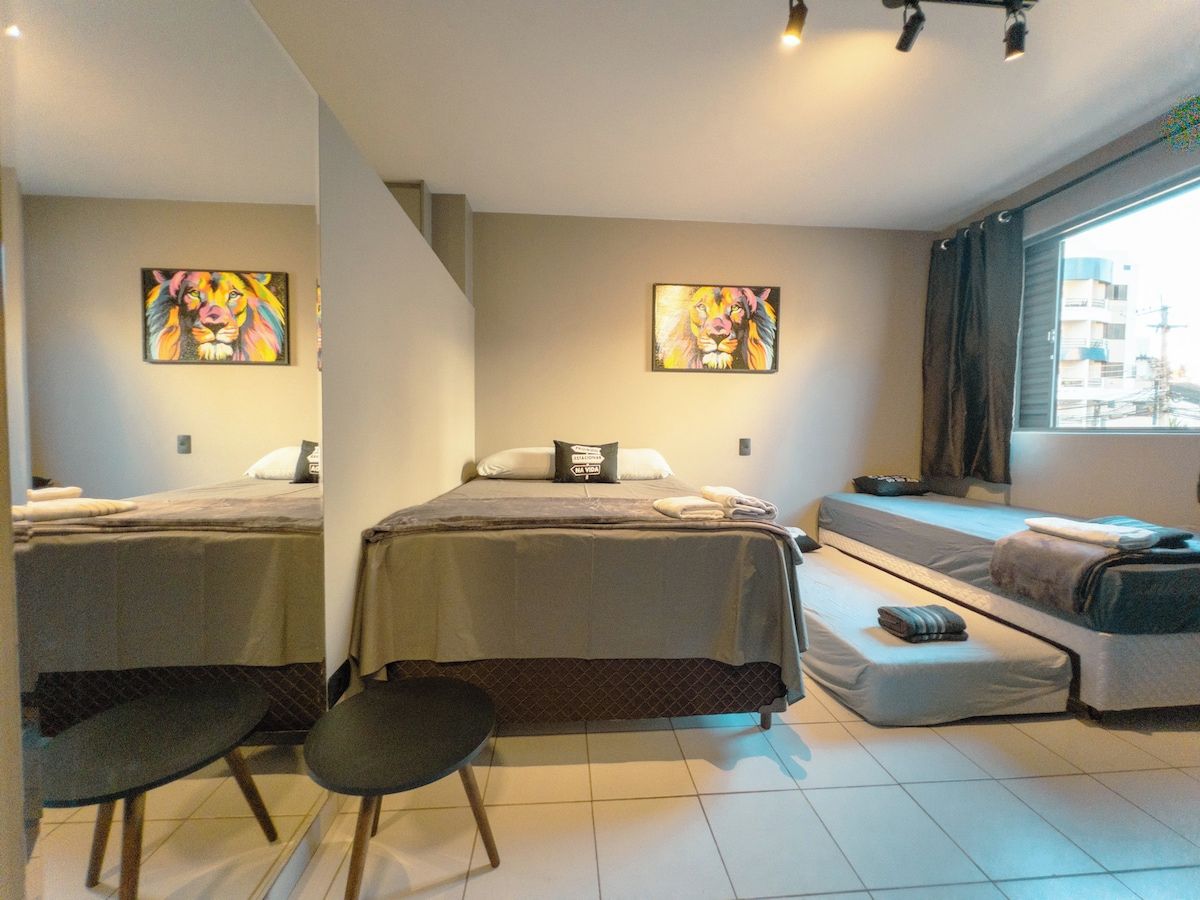 A hotel room with two beds, a sofa bed, a small table, and artwork on the walls.