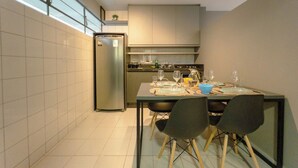 A modern kitchen with a dining table set for four, a refrigerator, and a window providing natural light. - Modern Apartment near UEM with Wi-Fi - LP12 (Maringá)