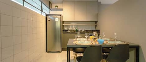 Una cocina moderna con una mesa de comedor para cuatro personas, un refrigerador y un ventanal que proporciona luz natural.