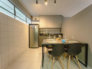 Eine moderne Küche mit Esstisch für vier Personen, einem Kühlschrank und einem Fenster mit Tageslicht.