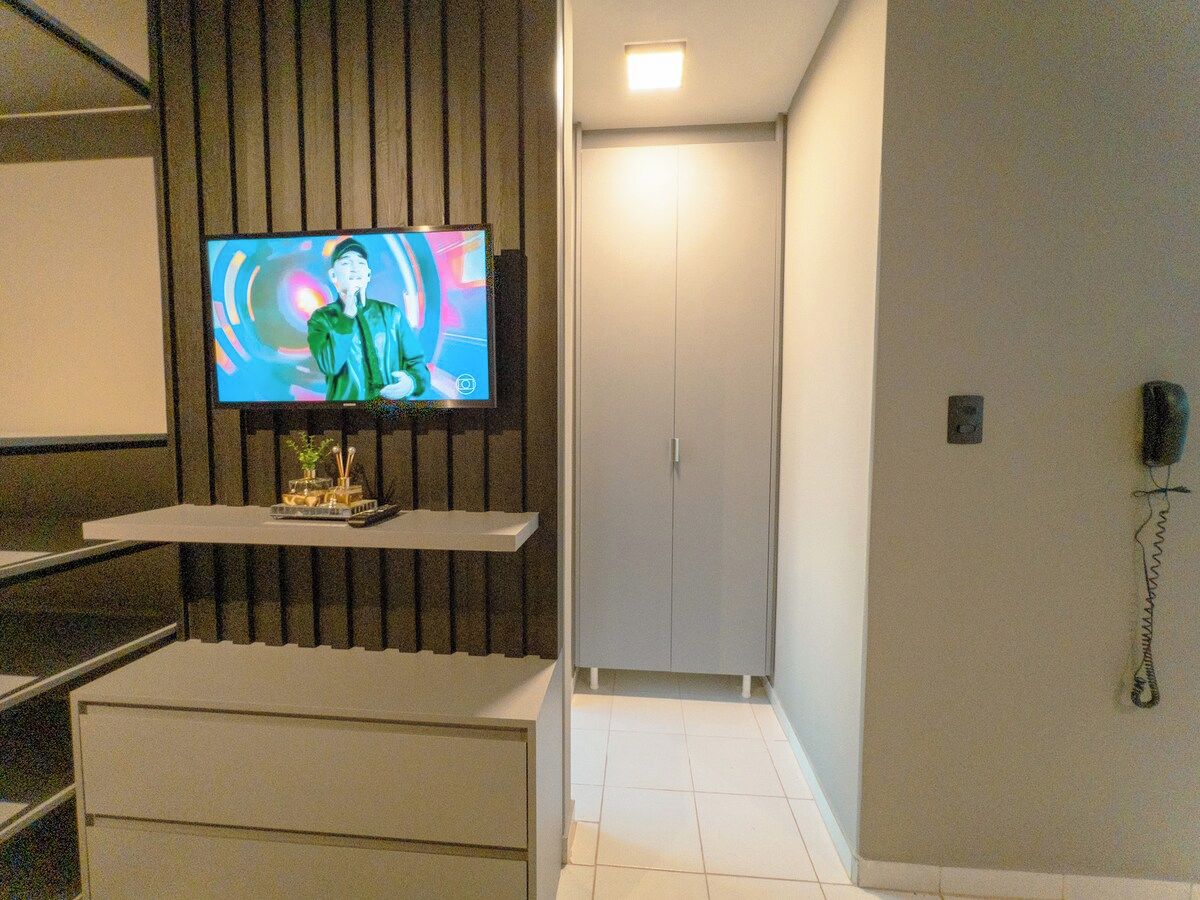 A hotel room with a television mounted on a wall, a small table with a decorative item, a wardrobe, and a telephone on the wall.