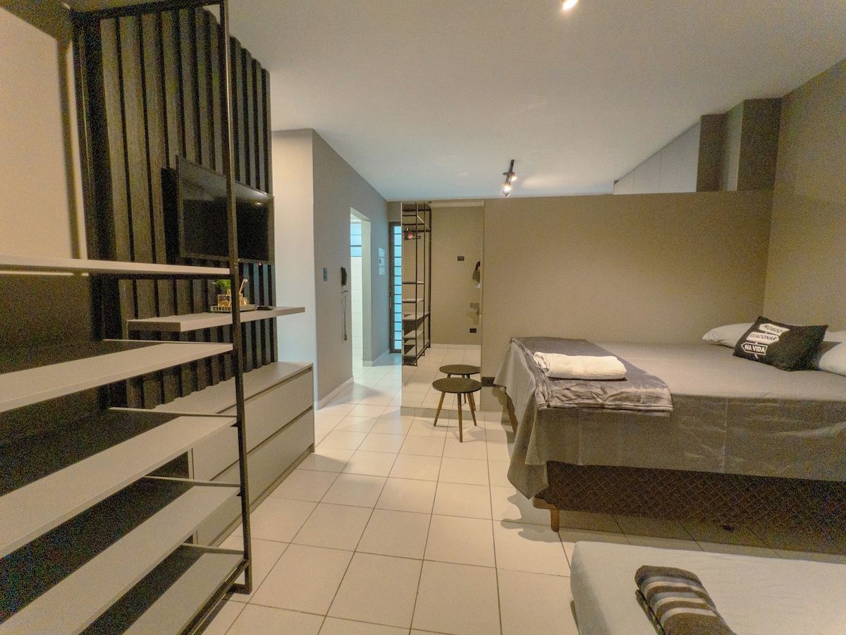 Une chambre d’hôtel moderne, équipée d’un lit, d’une petite table, d’une chaise, d’un escalier et offrant une vue sur le couloir.