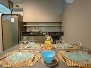 Une table à manger dressée avec des sets de table bleus et orange, des verres transparents et un pichet jaune.