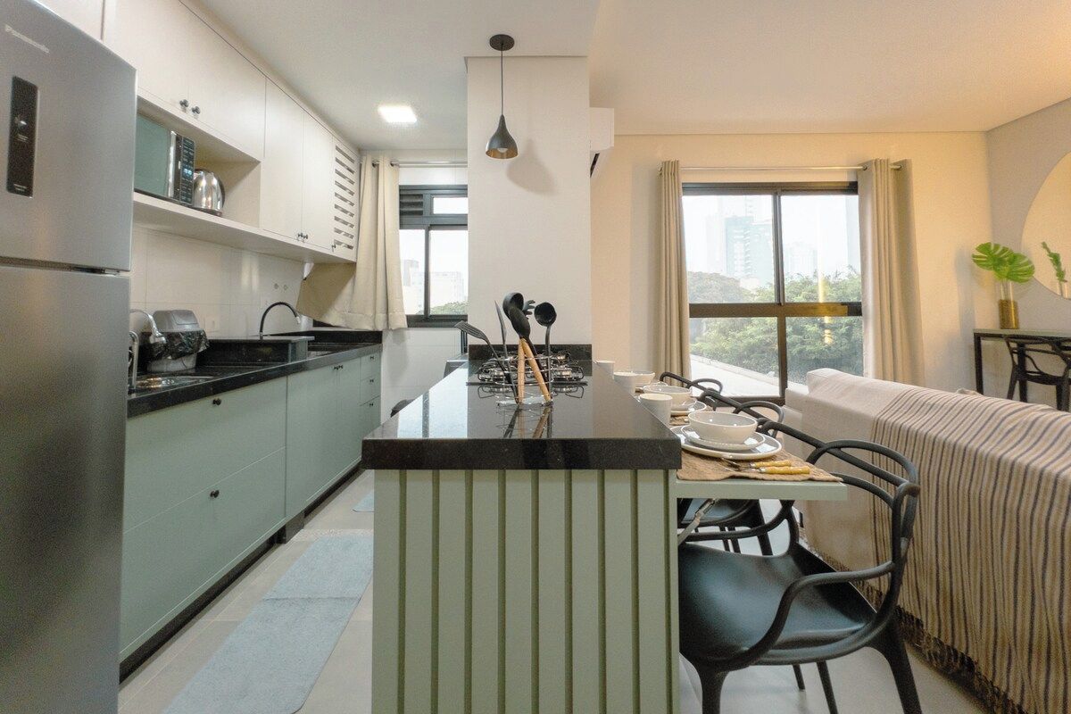A modern kitchen with a central island, dining area with chairs, and a large window with a city view.